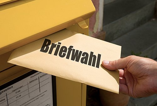 Symbolbild gelber Briefkasten mit Kuvert und Aufschrift Briefwahl