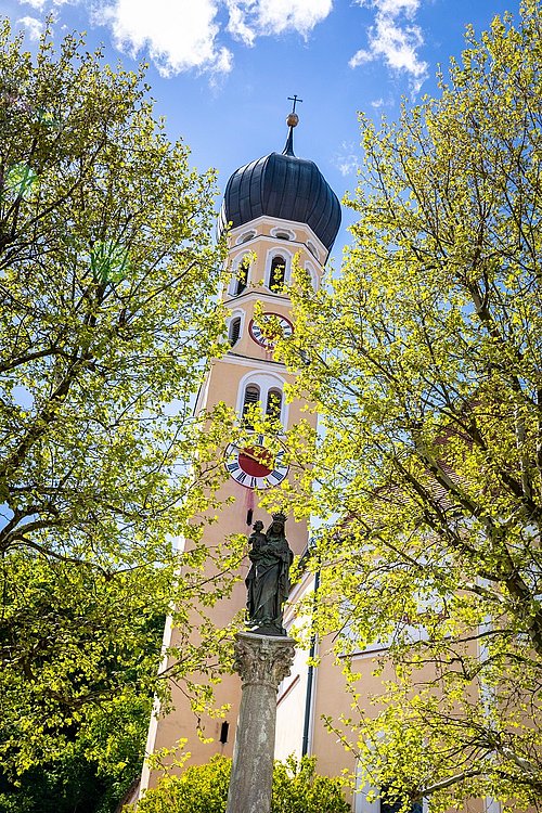 Kirche St. Andreas im Frühling mit Mariensäule im Vordergrund